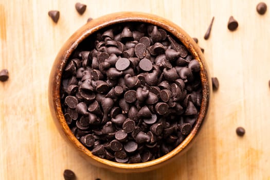 Directly above view of chocolate chips in bowl on wooden cutting board. unaltered, sweet food and unhealthy eating concept.