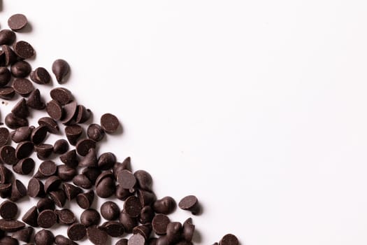 Overhead view of fresh chocolate chips scattered by copy space on white background. unaltered, sweet food and unhealthy eating concept.