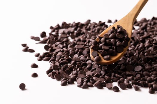 Close-up of wooden spoon with chocolate chips against white background. unaltered, sweet food and unhealthy eating concept.