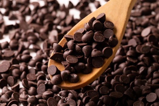 Close-up of fresh chocolate chips with wooden spoon. unaltered, sweet food and unhealthy eating concept.