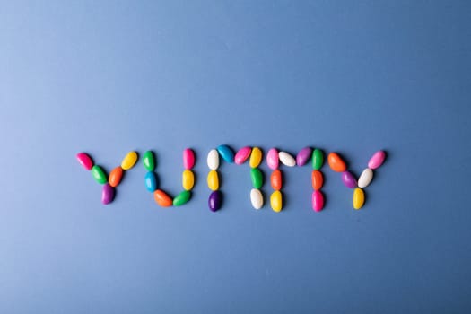 Overhead view of multi colored candies arranged as yummy word on blue background with copy space. unaltered, sweet food and unhealthy eating concept.