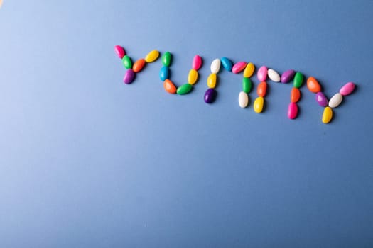 Overhead view of yummy word arranged from colorful candies on blue background over copy space. unaltered, sweet food and unhealthy eating concept.