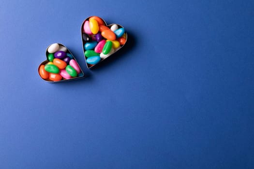 Directly above view of heart shape containers with colorful candies by copy space on blue background. unaltered, sweet food and unhealthy eating concept.