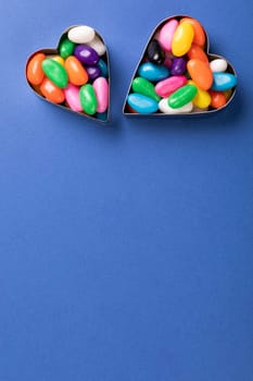 Overhead view of colorful candies inside heart shape containers over copy space on blue background. unaltered, sweet food and unhealthy eating concept.