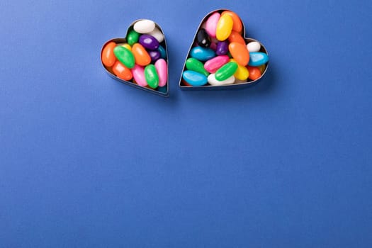 Directly above view of colorful candies in heart shape containers over copy space on blue background. unaltered, sweet food and unhealthy eating concept.