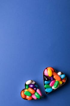 Overhead view of copy space above colorful candies in heart shape containers over blue background. unaltered, sweet food and unhealthy eating concept.