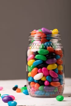 Close-up of multi colored candies in glass jars against gray background with copy space. unaltered, sweet food and unhealthy eating concept.