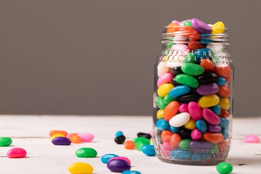 Close-up of full glass jar with multi colored candies against gray background with copy space. unaltered, sweet food and unhealthy eating concept.