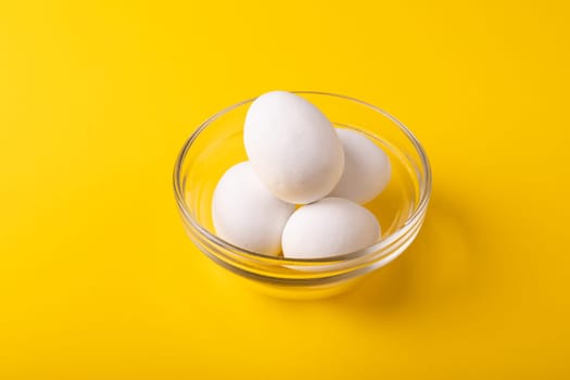 High angle view of fresh white eggs in glass bowl by copy space on yellow background. unaltered, food, healthy eating concept.