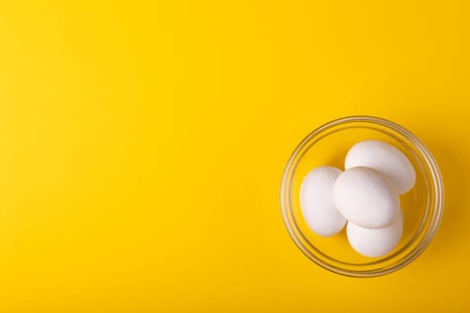 Directly above view of fresh white eggs in glass bowl by copy space on yellow background. unaltered, food, healthy eating concept.