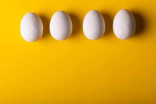 Overhead view of fresh white eggs arranged side by side on yellow background with copy space. unaltered, food, healthy eating concept.