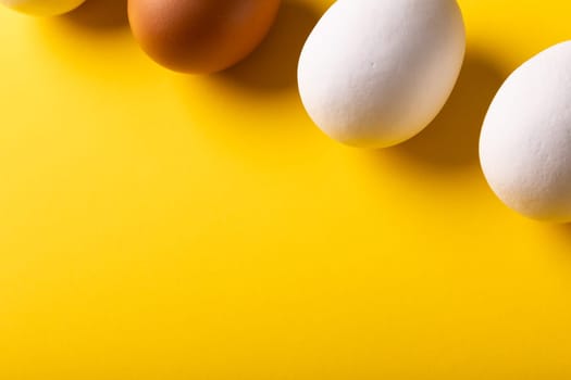 High angle close-up view of fresh white and brown eggs by copy space on yellow background. unaltered, food, healthy eating concept.