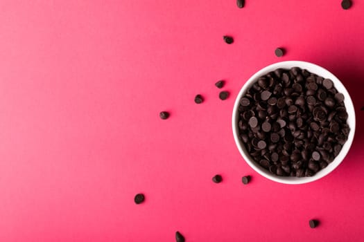 Overhead view of bowl with fresh chocolate chips by copy space over pink background. unaltered, sweet food and unhealthy eating concept.