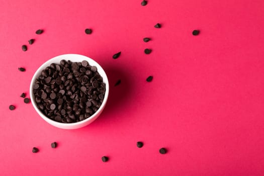 Directly above view of bowl with fresh chocolate chips scattered by copy space over pink background. unaltered, sweet food and unhealthy eating concept.