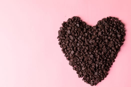 Directly above view of chocolate chips arranged as heart shape over pink background with copy space. unaltered, sweet food and unhealthy eating concept.