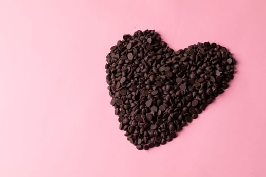 High angle view of fresh chocolate chips arranged heart shape by copy space against pink background. unaltered, sweet food and unhealthy eating concept.