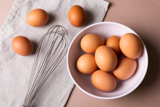 Directly above view of fresh brown eggs in bowl by wire whisk on napkin over table. unaltered, food, healthy eating concept.