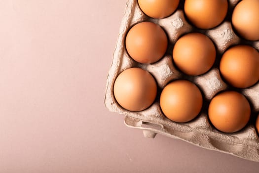 Directly above view of fresh brown eggs in carton by copy space over colored background. unaltered, food, healthy eating concept.