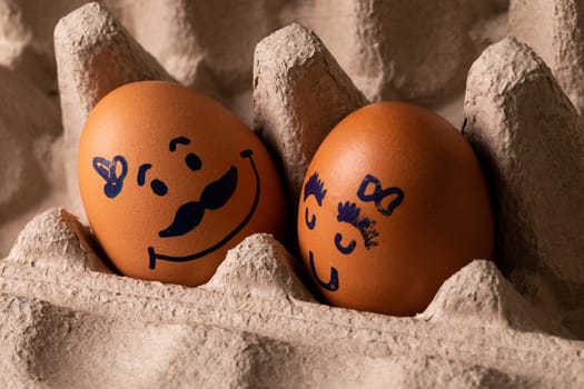 Close-up of creative male and female drawing on brown eggs in carton. unaltered, food, healthy eating, creative, humor concept.