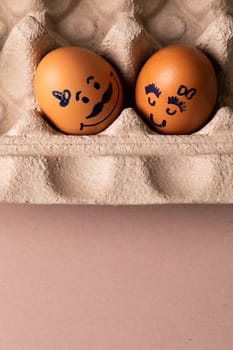 Close-up of creative female and male drawing on brown eggs in carton. unaltered, food, healthy eating, creative, humor concept.