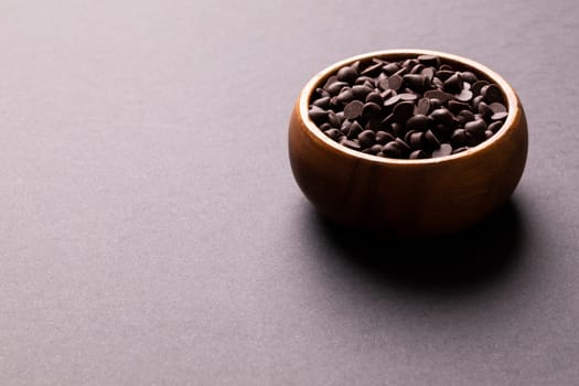 High angle view of fresh chocolate chips in wooden bowl against colored background with copy space. unaltered, sweet food and unhealthy eating concept.