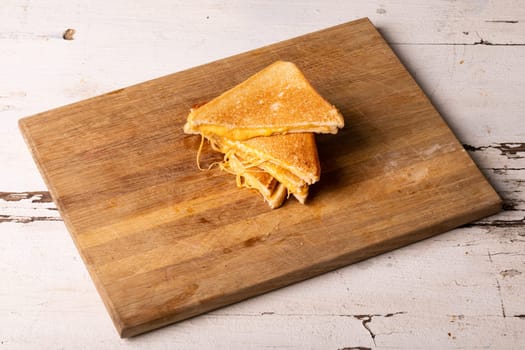 High angle view of fresh cheese sandwich served on wooden brown serving board over white table. unaltered, food, unhealthy eating and snack concept.