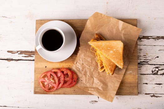 Overhead view of fresh cheese sandwich with tomato slices and black coffee on serving board. unaltered, food, unhealthy eating and snack concept.