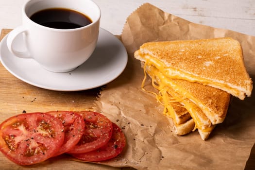 High angle view of fresh black coffee with tomato slices by cheese sandwich on wax paper. unaltered, food, unhealthy eating and snack concept.