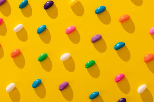 Full frame shot of multi colored candies arranged in a row on yellow background. unaltered, sweet food and unhealthy eating concept.