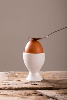 Close-up of spoon on fresh boiled brown egg in cup on table against gray background with copy space. unaltered, food, healthy eating and organic concept.