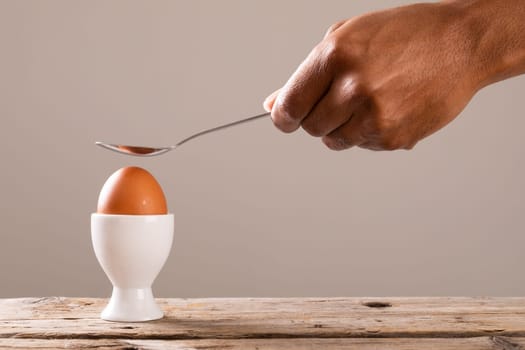 Cropped hand holding spoon over boiled brown egg in cup on table. unaltered, food, healthy eating and organic concept.