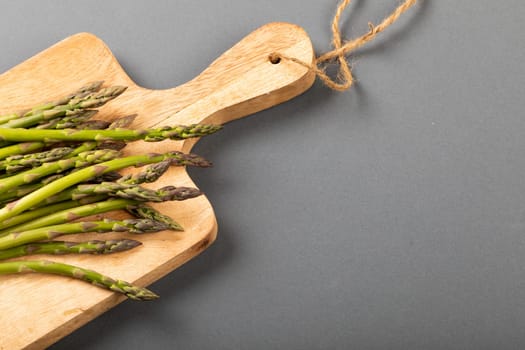 High angle view of fresh asparagus on wooden cutting board by copy space against gray background. unaltered, food, healthy eating and organic concept.