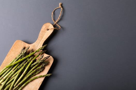 Overhead view of fresh asparagus on wooden cutting board by copy space against gray background. unaltered, food, healthy eating and organic concept.