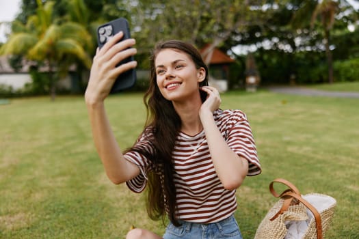 woman browsing young caucasian talk application happy tree t-shirt working park blogger phone call lifestyle smiling cellphone adult grass smartphone palm nature