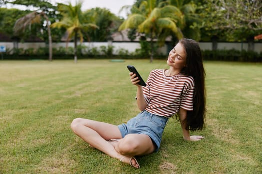 woman jeans bag nature browsing cellphone working happy lifestyle girl application talk blogger tree palm beautiful smiling summer phone park grass seasonal