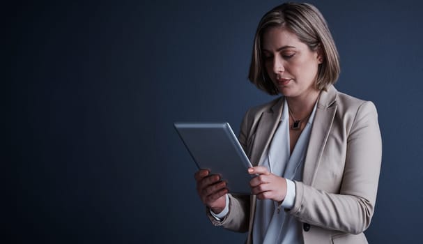 Everything is just a tap away. Studio shot of an attractive young corporate businesswoman using a tablet against a dark background