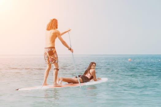 Sea woman and man on sup. Silhouette of happy young woman and man, surfing on SUP board, confident paddling through water surface. Idyllic sunset. Active lifestyle at sea or river