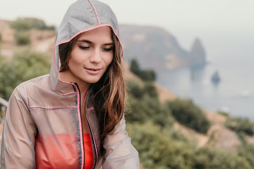 Woman rain park. Happy woman portrait wearing a raincoat with transparent umbrella outdoors on rainy day in park near sea. Girl on the nature on rainy overcast day