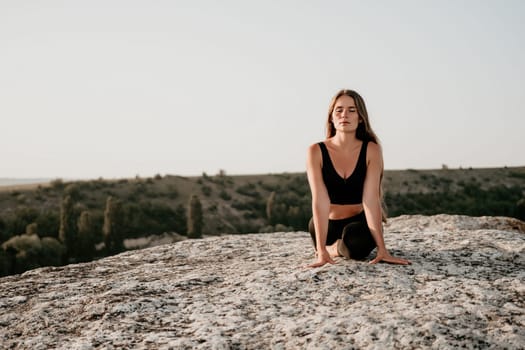 Well looking middle aged woman with long hair, fitness instructor in leggings and tops doing stretching and pilates on the rock near forest. Female fitness yoga routine concept. Healthy lifestyle.