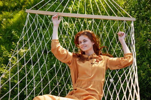 a beautiful, elegant woman lies in a long orange dress on a mesh hammock resting in nature, illuminated by the warm sunset light, smiling happily. Horizontal photo taken from above. High quality photo