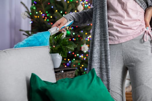 From the back of the sofa, a woman sweeps dust with a fine brush. Thorough cleaning for special occasions.