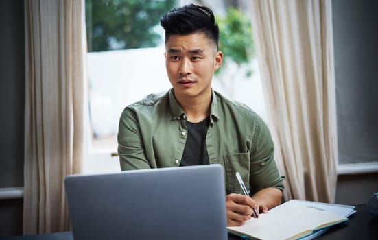 Hes in the zone. a handsome young man taking notes while working on his laptop at home