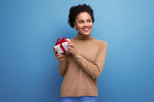 young happy latin woman with curly hair rejoices with a birthday present and isolated studio background with copy space.