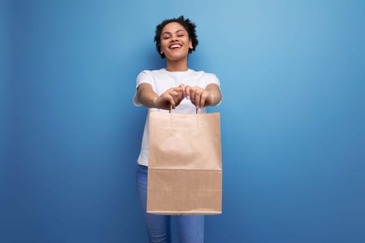 young happy brunette woman with afro hair in a white tank top holding a craft pait from a delivery service.