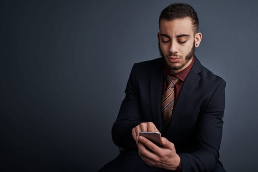 Its communication made simple. Studio shot of a stylish young businessman sending a text message while sitting against a gray background