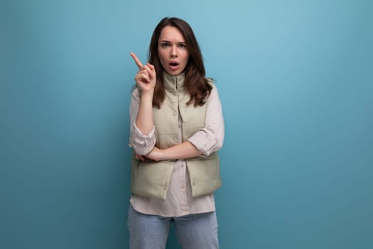 positive young brunette lady showing inspiration with hand on studio background with copy space.