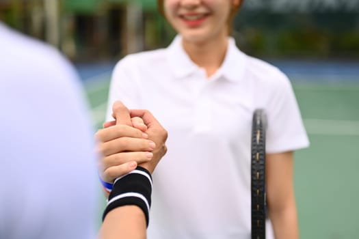 Smiling female tennis players shaking hands with competitor over net at tennis court after the match.