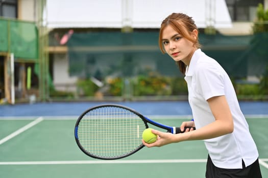 Determined young female tennis player with racket serving ball during match. Outdoor sports and healthy lifestyle concept.