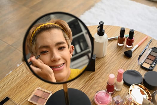 Smiling Asian gay man blogger filming daily makeup routine tutorial on smartphone. LGBTQ, domestic life and beauty concept.