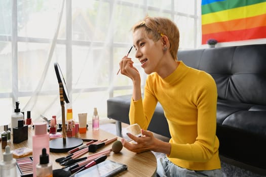 Smiling Asian gay man blogger filming daily makeup routine tutorial on smartphone. LGBTQ, domestic life and beauty concept.